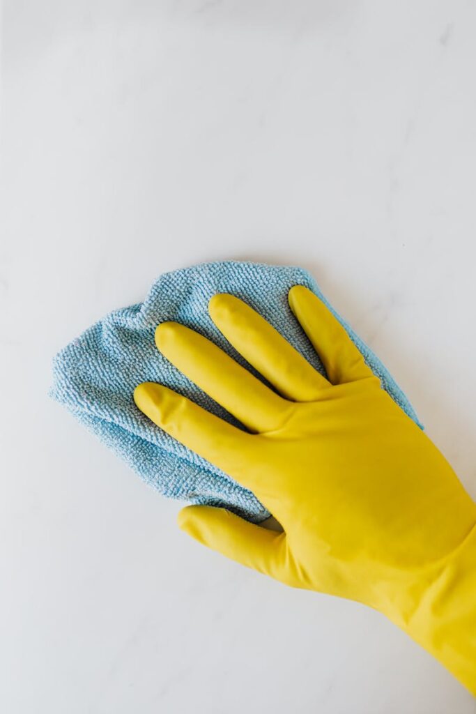 Yellow gloved hand wiping surface with blue cloth, concept of cleaning and hygiene.